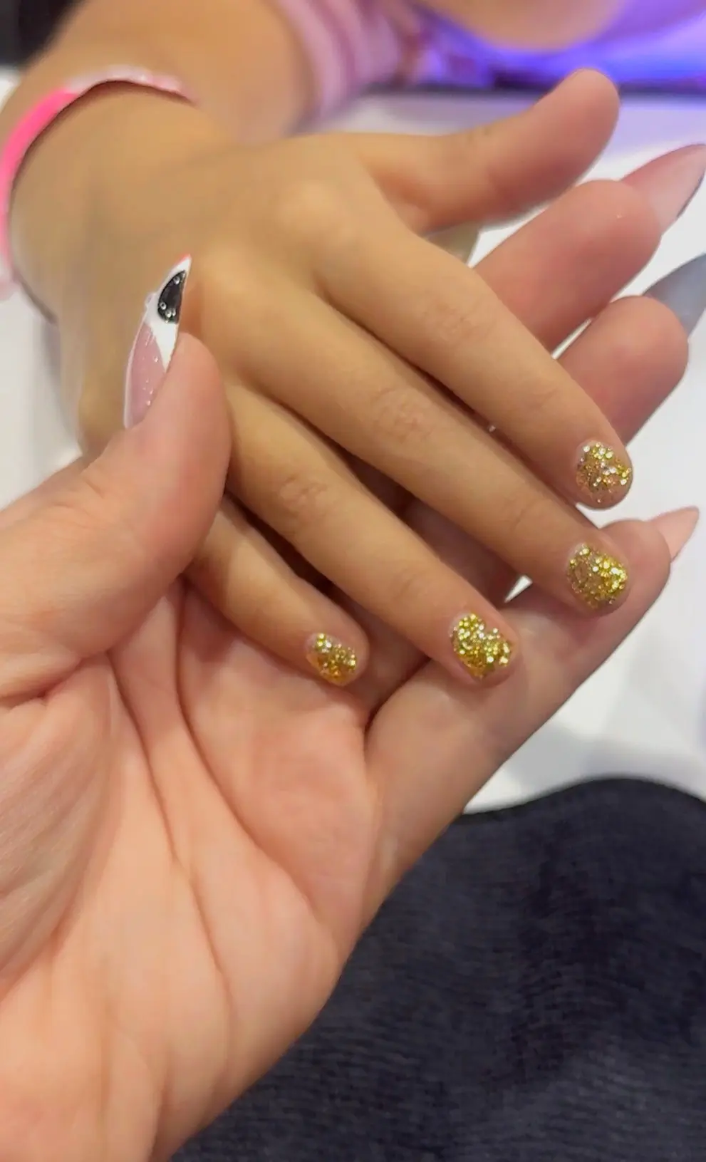 Manicure de gel con brillo dorado en uñas cortas, trabajo de estudiante de tecnología de uñas en expo