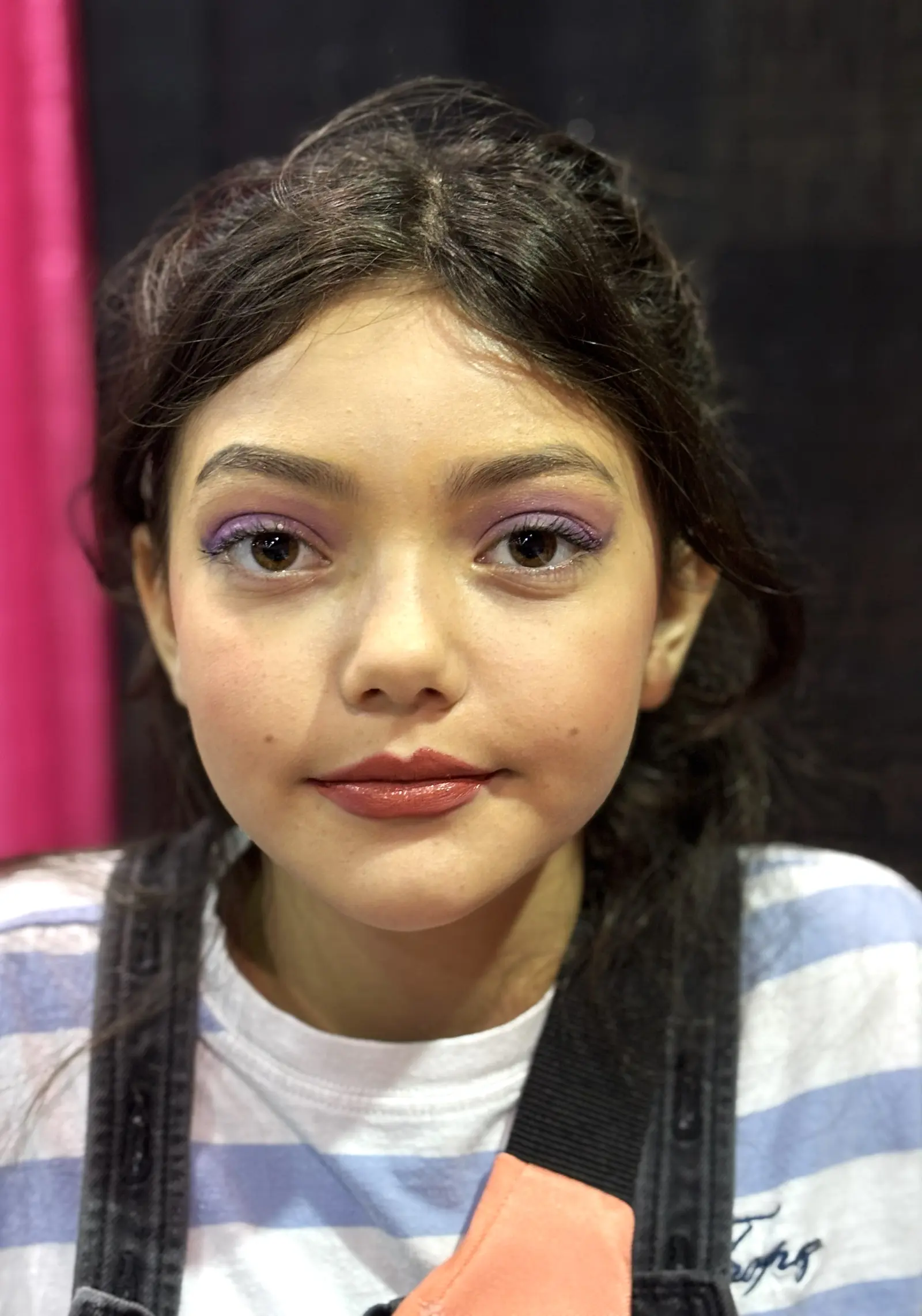 Maquillaje con sombra morada suave y labios brillantes, trabajo de estudiante en expo
