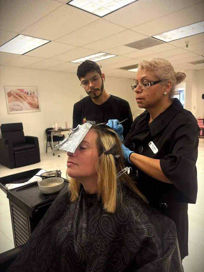 Un alumno de peluquería recibe orientación práctica sobre coloración capilar de la directora Maggie Serrano en Mima's Beauty College, en Phoenix, Arizona