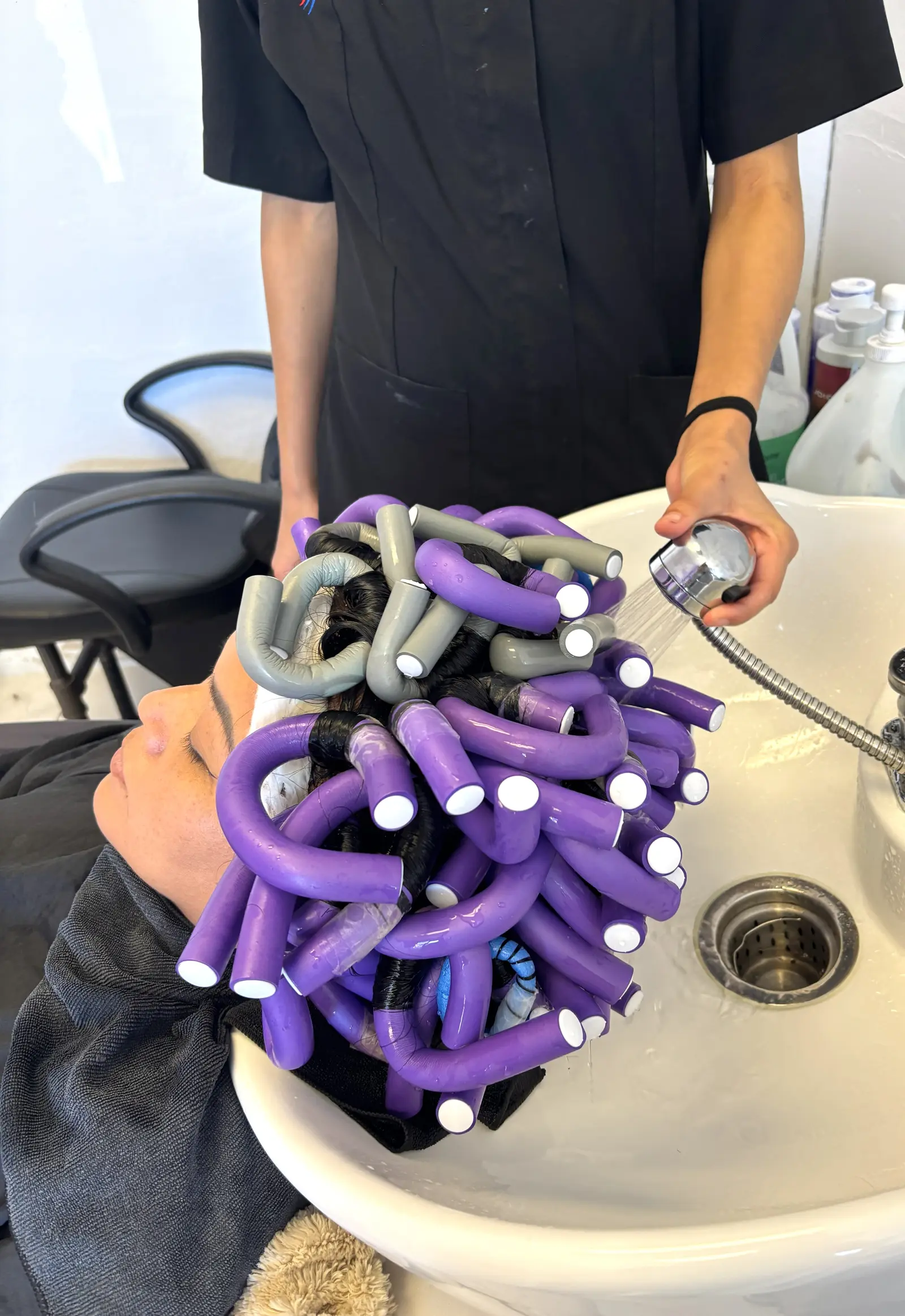 Estudiante enjuagando cabello envuelto en tubos de permanente en el lavabo del salón